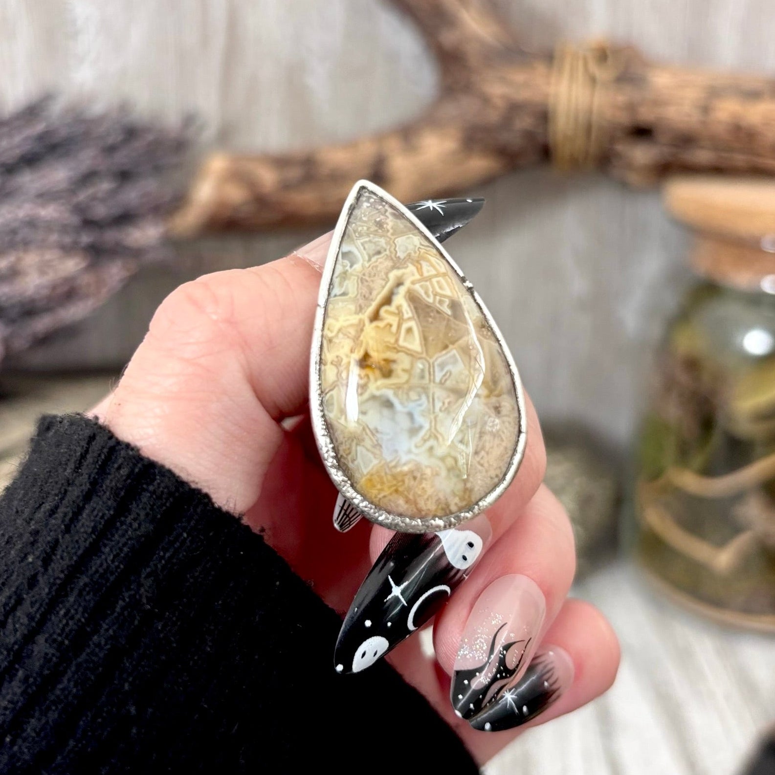 Teardrop-shaped stone pendant held by a hand with black nail polish against a neutral background.